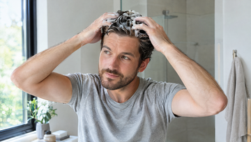 Man masseert minoxidil schuim in op zijn hoofdhuid in de badkamer